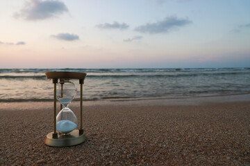 An hourglass lies on the sand on the beach with a beautiful sea background in the evening, passing...
