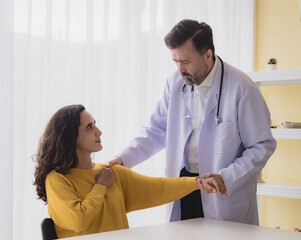 Fototapeta premium Portrait latin american woman sick injury with man doctor care caucasian physical therapist two people sitting talk helping support give advice and holding hand arm inside hospital room service