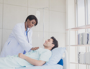 Portrait patient caucasian man lying bed with woman doctor African-American standing carer physical therapist two people talk helping support and check treat sick person inside hospital room service.