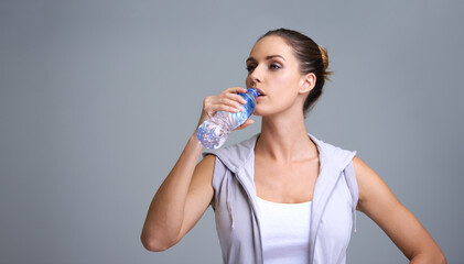 Woman, fitness and drinking water for hydration or natural sustainability on a gray studio background. Face of thirsty female person or athlete with mineral drink in rest, break or recovery on mockup