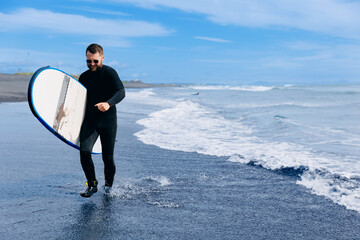 Extreme Surfer man in wetsuit with surfboard, winter surfing in ocean. North sea with sunlight, adventure travel sport concept