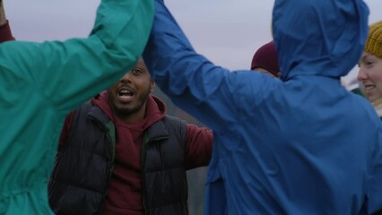 Group of diverse tourists have fun together during vacation. Multiethnic big family dance on the hilltop resting outdoors. Mountains landscape and forest in the background. Tourism and active leisure.