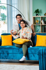 Obraz premium Happy Indian young boy sitting on sofa with older mother, enjoying coffee, tea in living room.