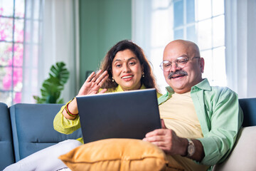 Young and happy Indian couple sitting on sofa at home, using a laptop for video call.