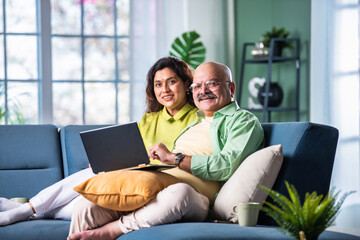 Young and happy Indian couple sitting on sofa at home, using a laptop for video call.