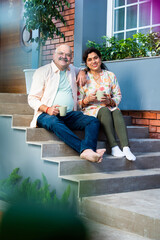 Obraz premium Indian Cheerful old couple having coffee at home while sitting on sofa or staircase