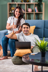 Young and happy Indian couple sitting on sofa at home, using a laptop for shopping or video call.