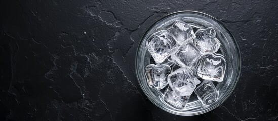 A glass filled with ice cubes on a dark surface