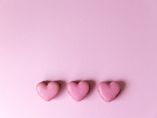 Three heart shaped pink macaron cookies on bright pink background