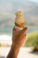 Hand holding vanilla ice cream in a cone against nature background