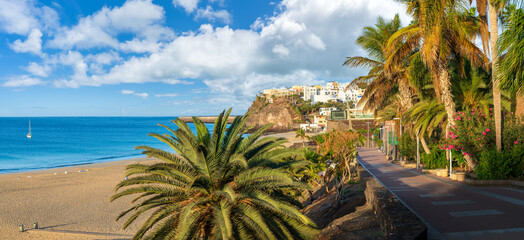Stroll along Morro Jable palm-lined promenade in Fuerteventura, with azure waters and sandy shores offering a tranquil Canary Island escape