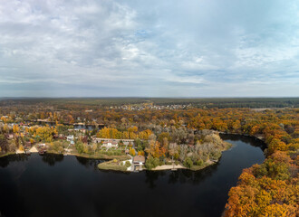 Aerial panorama of autumn river with golden trees forest. Flying above vibrant autumnal village in Ukraine