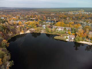 Fototapeta na wymiar Aerial autumn cottages on river with colorful forest. Flying above vibrant autumnal village in Ukraine