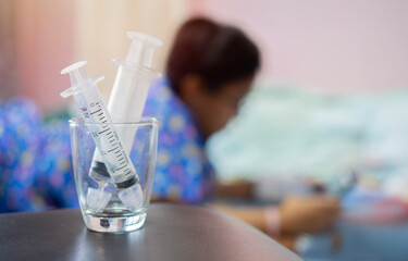 A syringes of normal saline use to clean up for nose in glass on table in front of out of focus...