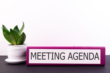MEETING AGENDA Office folder on a dark desktop with a flower on a light background
