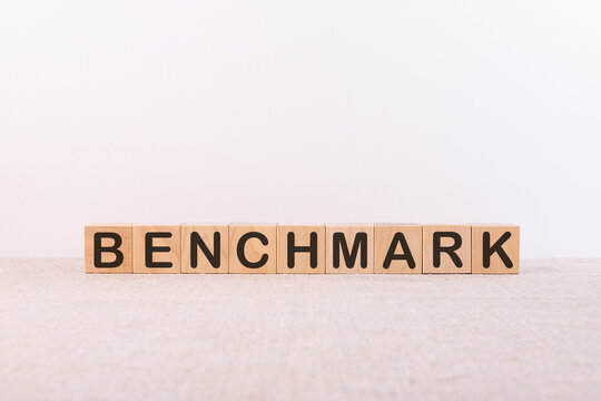Benchmark word concept written on wooden building cubes on a light table and light background