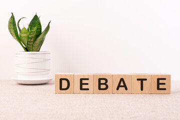 Debate word concept on wooden cubes on a table with flower and light background