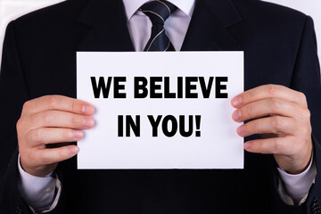 Businessman holding a card with text we believe in you