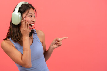  Beautiful young asian woman wearing headphones, pointing finger at the right side of the photo...