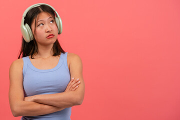  Young thoughtful Chinese woman isolated on pink background listening to music.