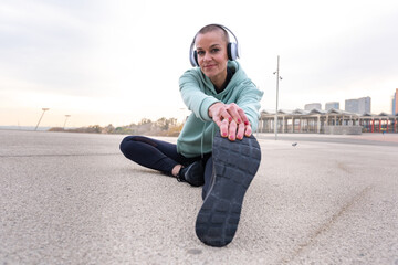 Sporty woman with sports headphones doing stretching sitting concentrated looking at camera. - Powered by Adobe