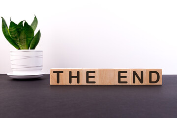 The end word concept on wooden blocks on a black table with a green flower on a white background