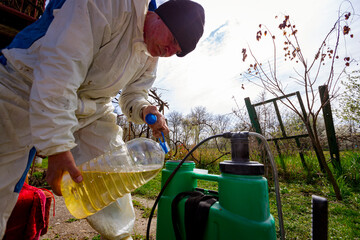 Farmer is pouring substance for sprinkling fruit trees in plastic knapsack sprayer