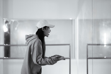 Young woman in cap practicing break dancing in dance studio. Black and white tone