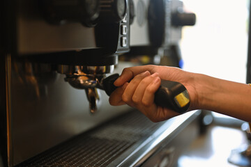 Cropped shot of barista using coffee machine, making espresso for client in a trendy cafe