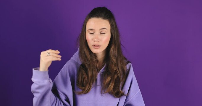 Brunette indignant woman showing blah blah blah gesture with hands isolated on studio purple background. Empty promises, blah concept. Lier, not interested. Annoyed girl making bla bla hand gesture.