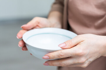 Unrecognizable woman holding empty bowl in her hands, kitchen interior, copy space, closeup shot,...