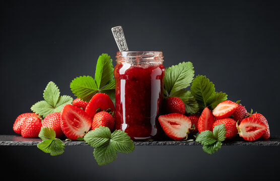 Strawberry jam and fresh berries on a black background.