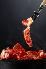 Fried steaming bacon slices on a black background.