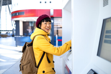 Female passenger with backpack buying train ticket at self-service machine.