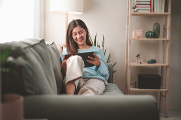 Obraz premium woman, happy, home, lifestyle, sofa, tablet, online, sitting, communication, young. beautiful woman relaxing on comfortable sofa with tablet, playing social or chatting online via social networks