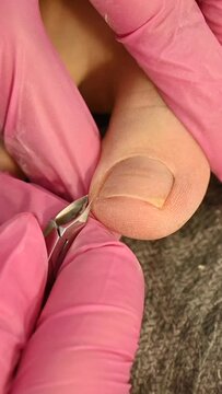 The master makes a pedicure with tweezers in a beauty salon. Vertical video.