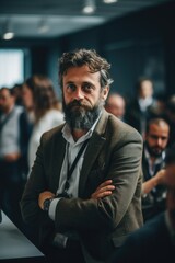 Fototapeta premium A man with a beard sitting in front of a group of people. Can be used to represent leadership, team meetings, or discussions