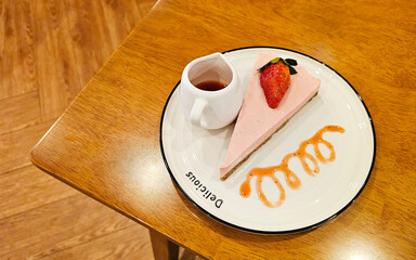 A delectable slice of strawberry cheesecake served with a side of sauce on a stylish plate