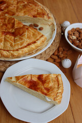  Galette des rois, traditional french cake with almond cream with a slice on a plate and festive decorations on wooden table. Epiphany cake