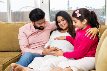 Happy indian couple expecting a baby while husband holding her hand and his daughter touching belly...