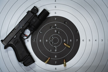 A shooting target with bullet holes in the center and a tactical pistol with a flashlight. © Dmitri