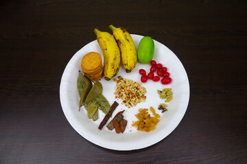 Tray of Ingredients Biscuits, Banana, Lemon, Bay Leaf, Cinnamon, Raisins, Almonds, Cardamom, Cloves, and Cherry Fruit 