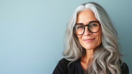 Woman with silver hair and glasses smiling against a light blue background.