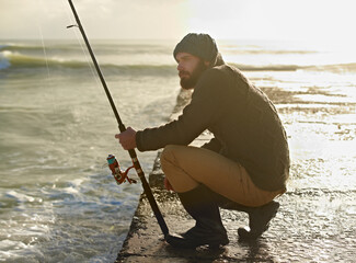 Man, thinking and fishing on beach in hobby, relax and sea for peace wellness on holiday. Fisherman, natural and vacation in cape town by ocean, adventure and nature by hook for fish to bite