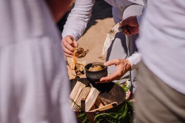 Jurmala, Latvia - july 25, 2023 - Hands holding a bark torch and a small cauldron over kindling and...