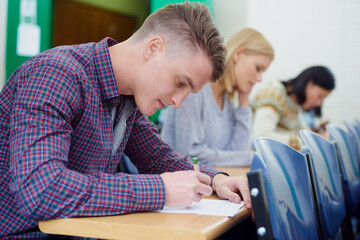 University student, desk and writing exam in classroom for education assessment for knowledge, diploma or scholarship. Men, woman and test in London lecture hall or study document, academy or college