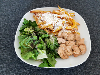Homemade grilled chicken with french fries, cheese and green salad, served on a white plate