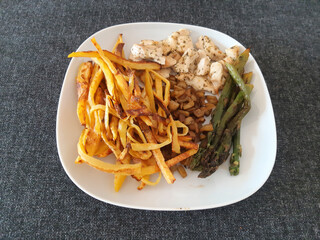 Homemade grilled chicken with french fries, eggplant and grilled asparagus, served on a white plate