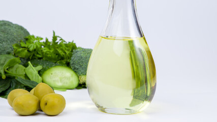 Olive oil in a bottle with green vegetables on a white background