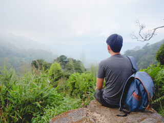 Asian man with backpack traveling solo on a tropical mountain peak in the morning